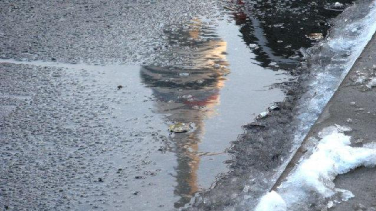 A puddle on a cold, wet street reflects a building resembling the Eiffel Tower. Snow and ice line the pavement, indicating winter conditions. The textured road surface adds detail to the scene. Waterproofing Company | Basement Leak Repair | City Wide Group | Professional waterproofing company and basement leak repair in Toronto since 1961. | https://www.citywidegroup.com | +1 416-283-5500