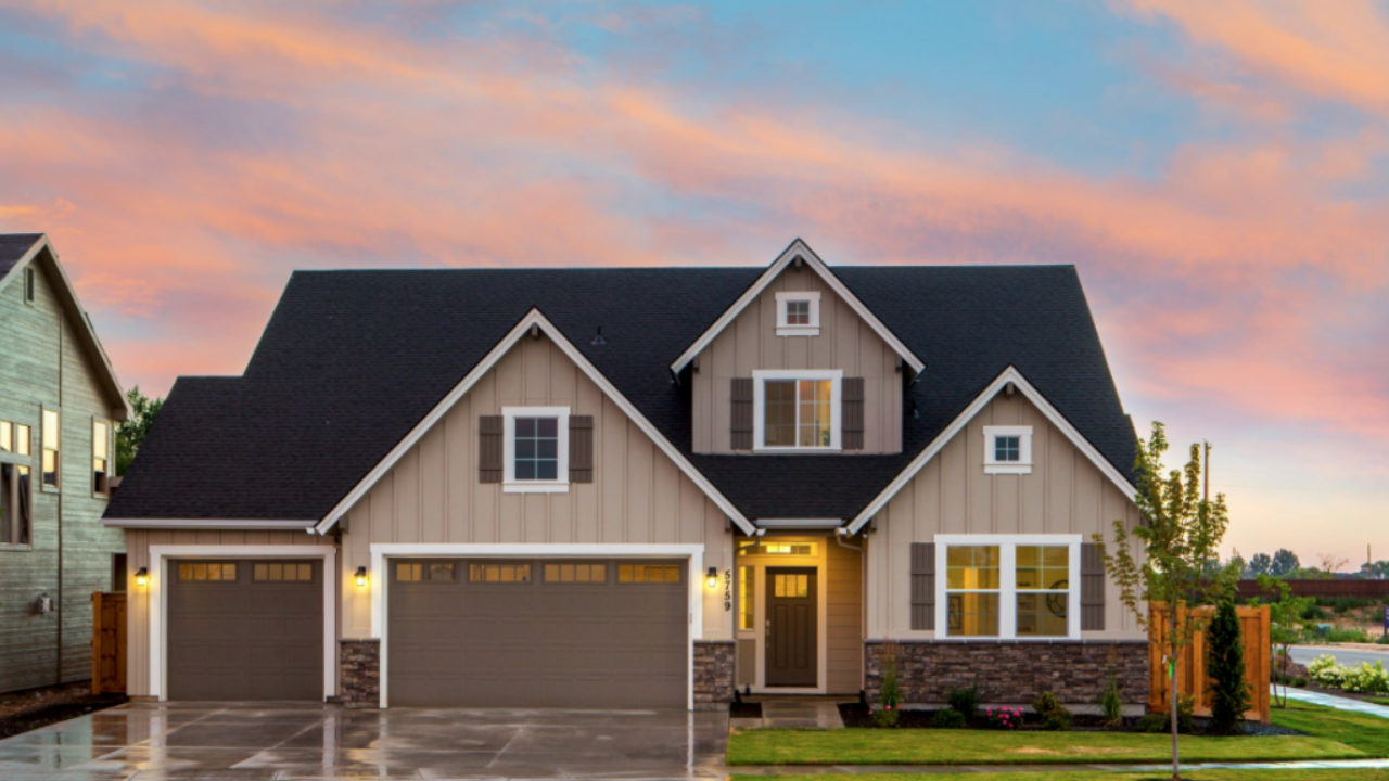 A modern suburban house with beige siding and a dark roof at dusk. It features two garages, lit exterior lights, and a small front lawn. The sky is vibrant with pink and blue hues. Waterproofing Company | Basement Leak Repair | City Wide Group | Professional waterproofing company and basement leak repair in Toronto since 1961. | https://www.citywidegroup.com | +1 416-283-5500