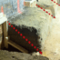 On a construction site, an excavated trench runs alongside a brick wall, supported by wooden braces. Red dashed lines highlight areas of concern or measurement. Dirt and debris scatter the ground—a scene that City Wide Group expertly navigates in their projects across town. Waterproofing Company | Basement Leak Repair | City Wide Group | Professional waterproofing company and basement leak repair in Toronto since 1961. | https://www.citywidegroup.com | +1 416-283-5500