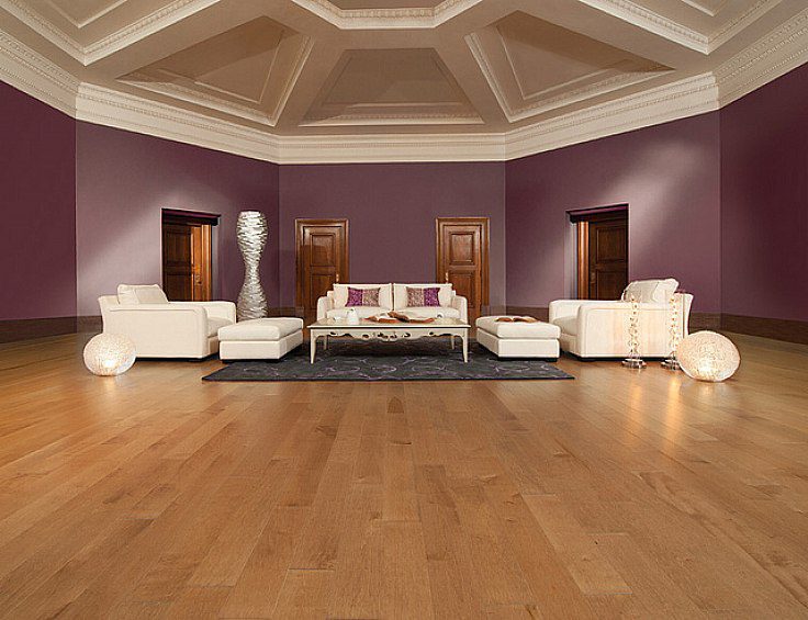 A spacious room with a wooden floor features modern white sofas and armchairs arranged around a central coffee table. The deep purple walls are accentuated by a coffered ceiling and several doorways, while artistic floor lamps provide soft lighting. Waterproofing Company | Basement Leak Repair | City Wide Group | Professional waterproofing company and basement leak repair in Toronto since 1961. | https://www.citywidegroup.com | +1 416-283-5500