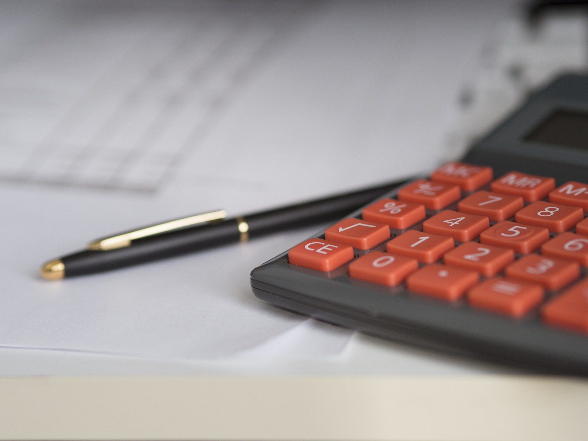 A calculator with red buttons sits on top of documents scattered on a desk. A black pen with a gold tip rests nearby. The scene suggests a work or study environment focused on calculations or financial tasks. Waterproofing Company | Basement Leak Repair | City Wide Group | Professional waterproofing company and basement leak repair in Toronto since 1961. | https://www.citywidegroup.com | +1 416-283-5500