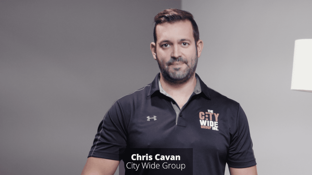 A man with short hair and a beard is wearing a black polo shirt emblazoned with a City Wide Group logo. He stands confidently against a plain gray backdrop, while the text overlay reads: Chris Cavan, making headlines at City Wide Group. Waterproofing Company | Basement Leak Repair | City Wide Group | Professional waterproofing company and basement leak repair in Toronto since 1961. | https://www.citywidegroup.com | +1 416-283-5500