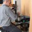 A person kneels on a cloth, expertly repairing plumbing under a sink for City Wide Group. Tools in hand, they focus on a cylindrical component, with wooden cabinetry open above them. Waterproofing Company | Basement Leak Repair | City Wide Group | Professional waterproofing company and basement leak repair in Toronto since 1961. | https://www.citywidegroup.com | +1 416-283-5500