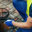 A worker in a neon yellow safety vest and blue gloves is kneeling on a cobblestone surface, using a tool to inspect or clean a round sewer opening with a metal cover. Waterproofing Company | Basement Leak Repair | City Wide Group | Professional waterproofing company and basement leak repair in Toronto since 1961. | https://www.citywidegroup.com | +1 416-283-5500