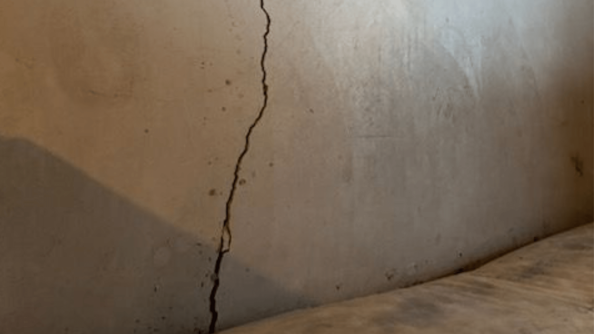 A cracked beige wall with a prominent vertical fissure running from the bottom up, next to a slightly slanted surface, possibly a floor or furniture. Waterproofing Company | Basement Leak Repair | City Wide Group | Professional waterproofing company and basement leak repair in Toronto since 1961. | https://www.citywidegroup.com | +1 416-283-5500