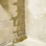 Water coming up through basement floor crack beside a damp concrete wall